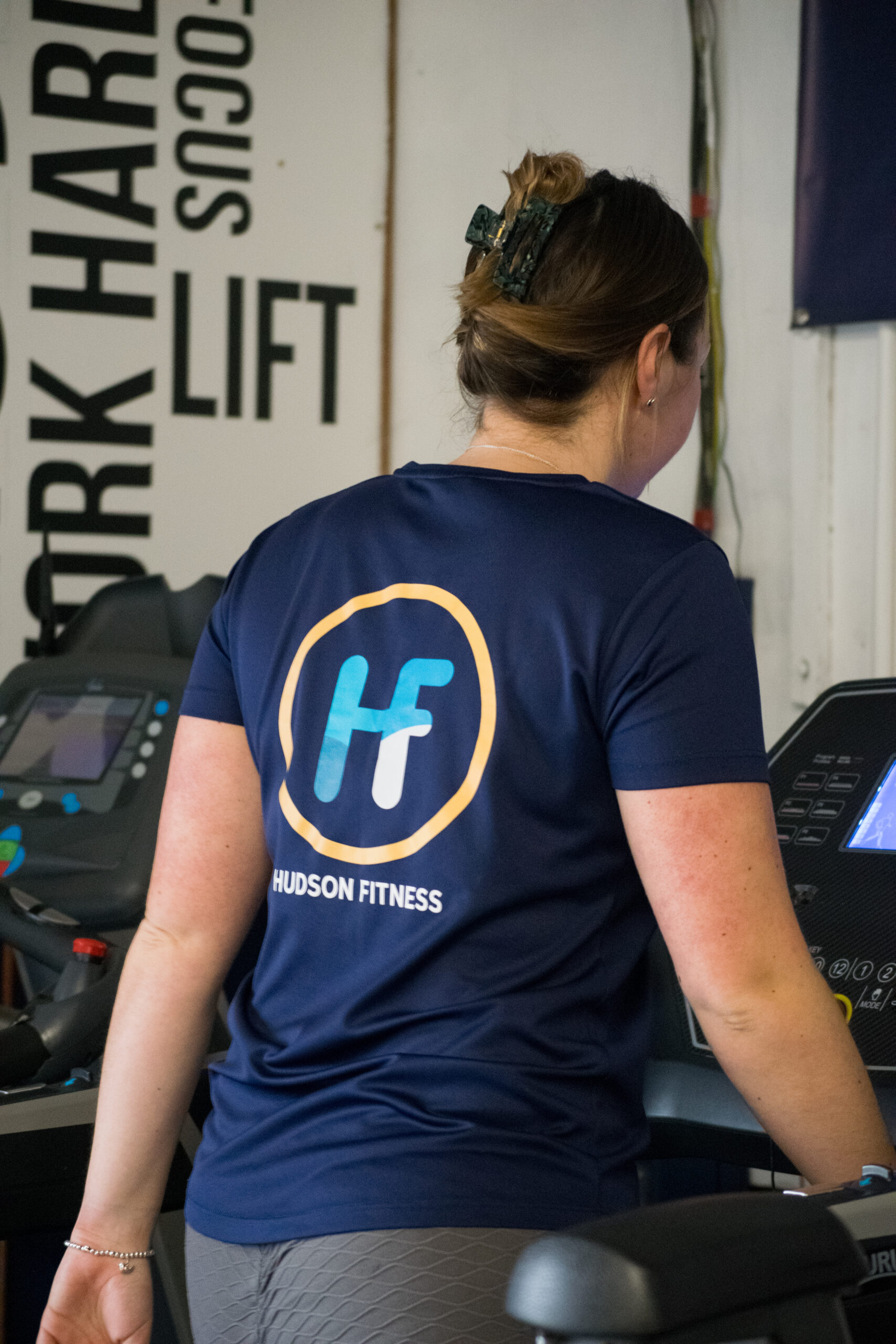 _DSC0060 Personal trainer wearing a navy Hudson Fitness branded t-shirt standing by treadmills in a gym